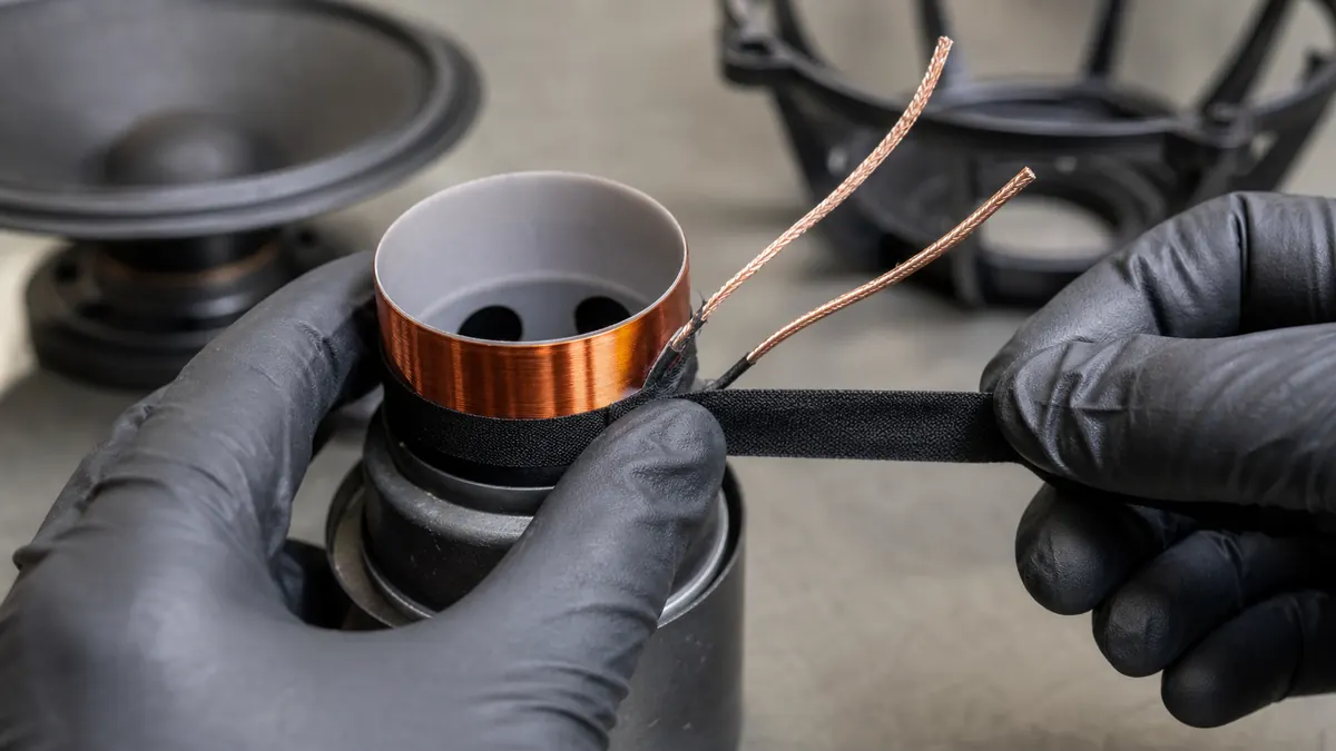 Loudspeaker technician wrapping narrow black acetate cloth tape around the copper voice coil lead transition on a speaker former